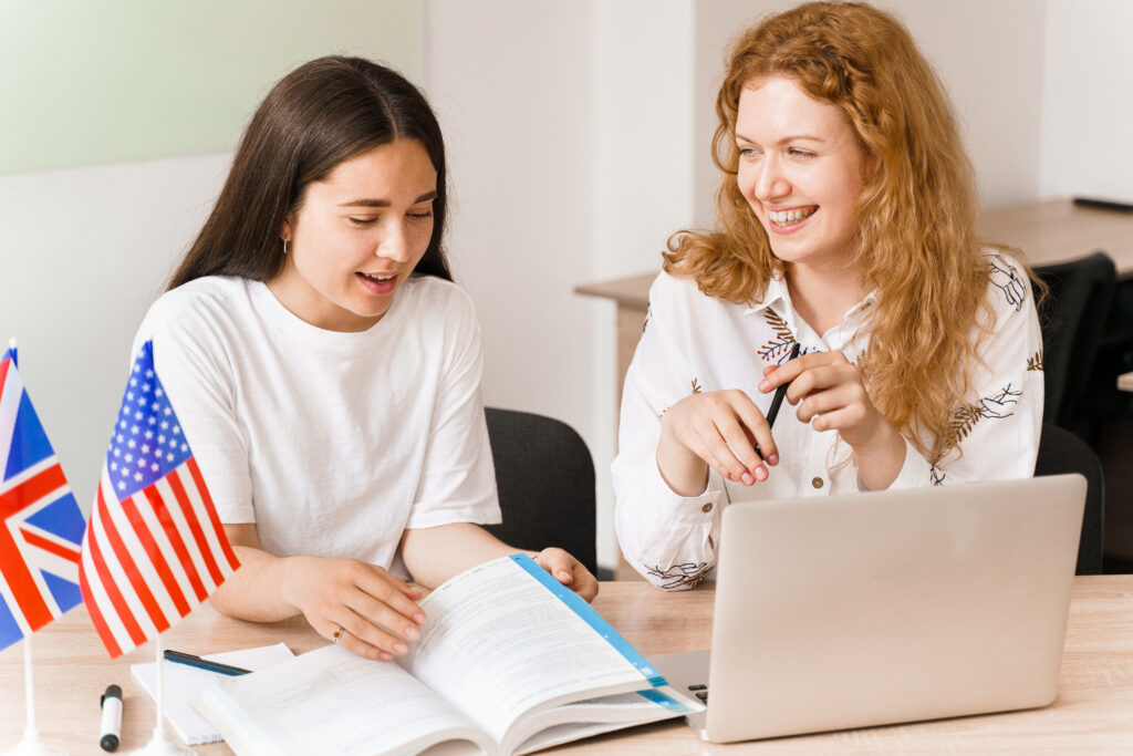 Uśmiechnięta nauczycielka języka angielskiego tłumaczy studentce gramatykę za pomocą laptopa